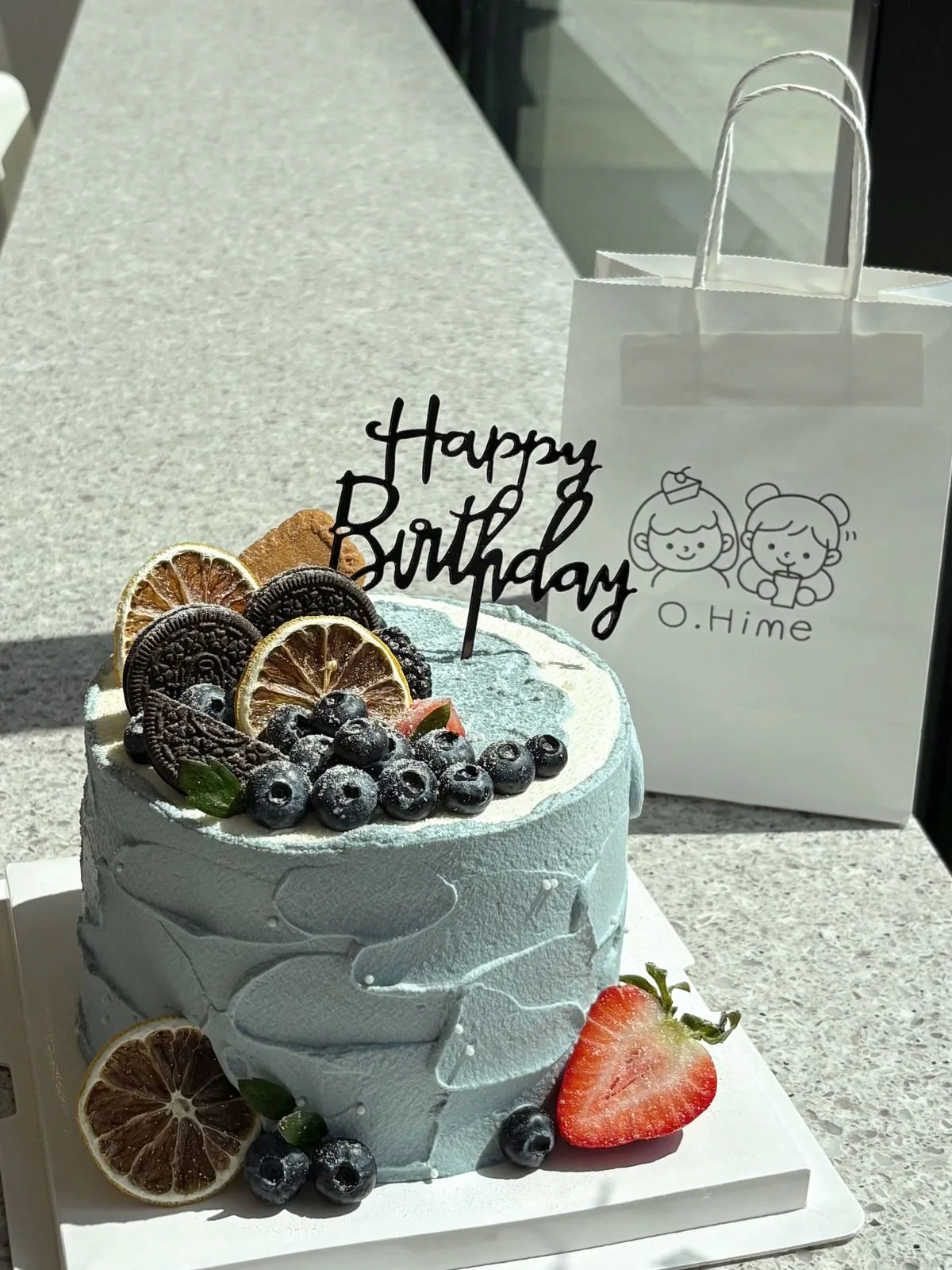 Light blue cream birthday cake with blueberries, cookies and birthday topper at O.Hime Cake, a Bakery in Waterloo
